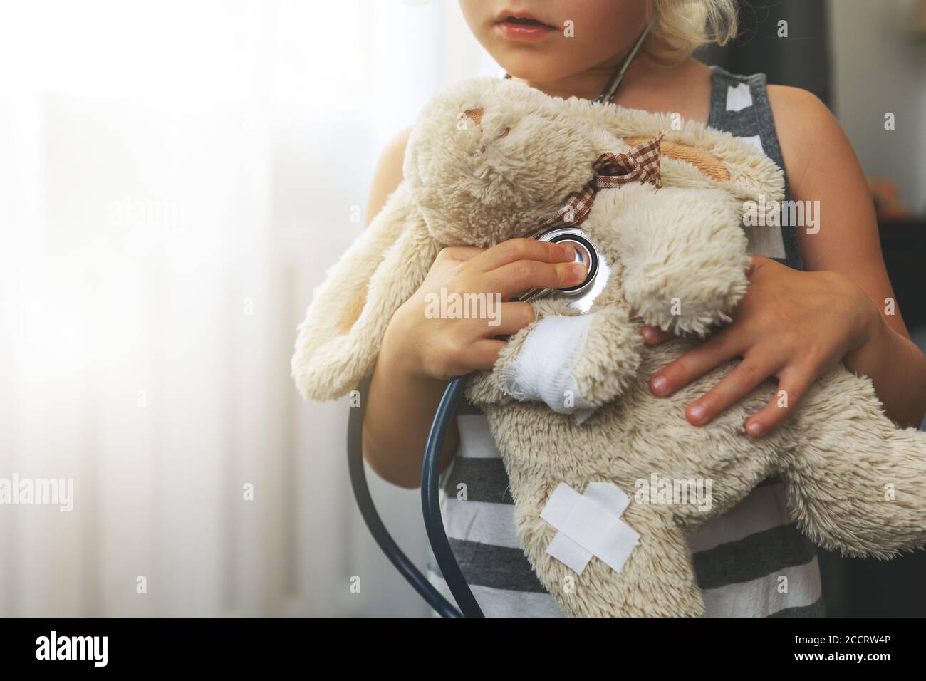 child playing doctor with soft toy. girl examining bunny with stethoscope at home Stock Photo
