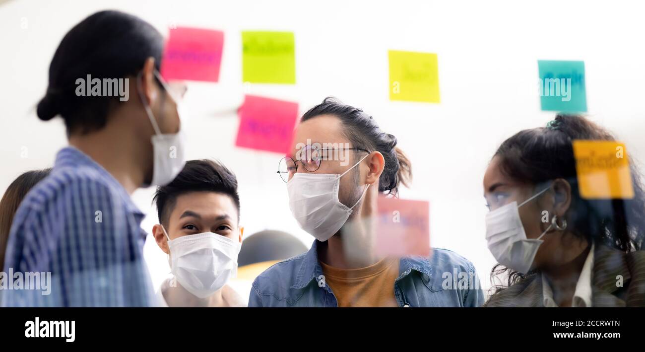 Panorama Interracial asian business team brainstorming idea at office meeting room after reopen due to coronavirus COVID-19. They wear face mask reduc Stock Photo