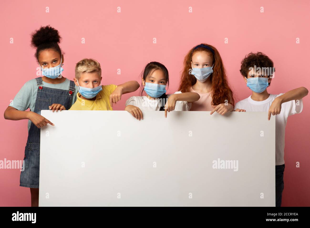 Multiethnic group of kids in medical masks pointing at blank banner on pink  background, mockup for design Stock Photo - Alamy