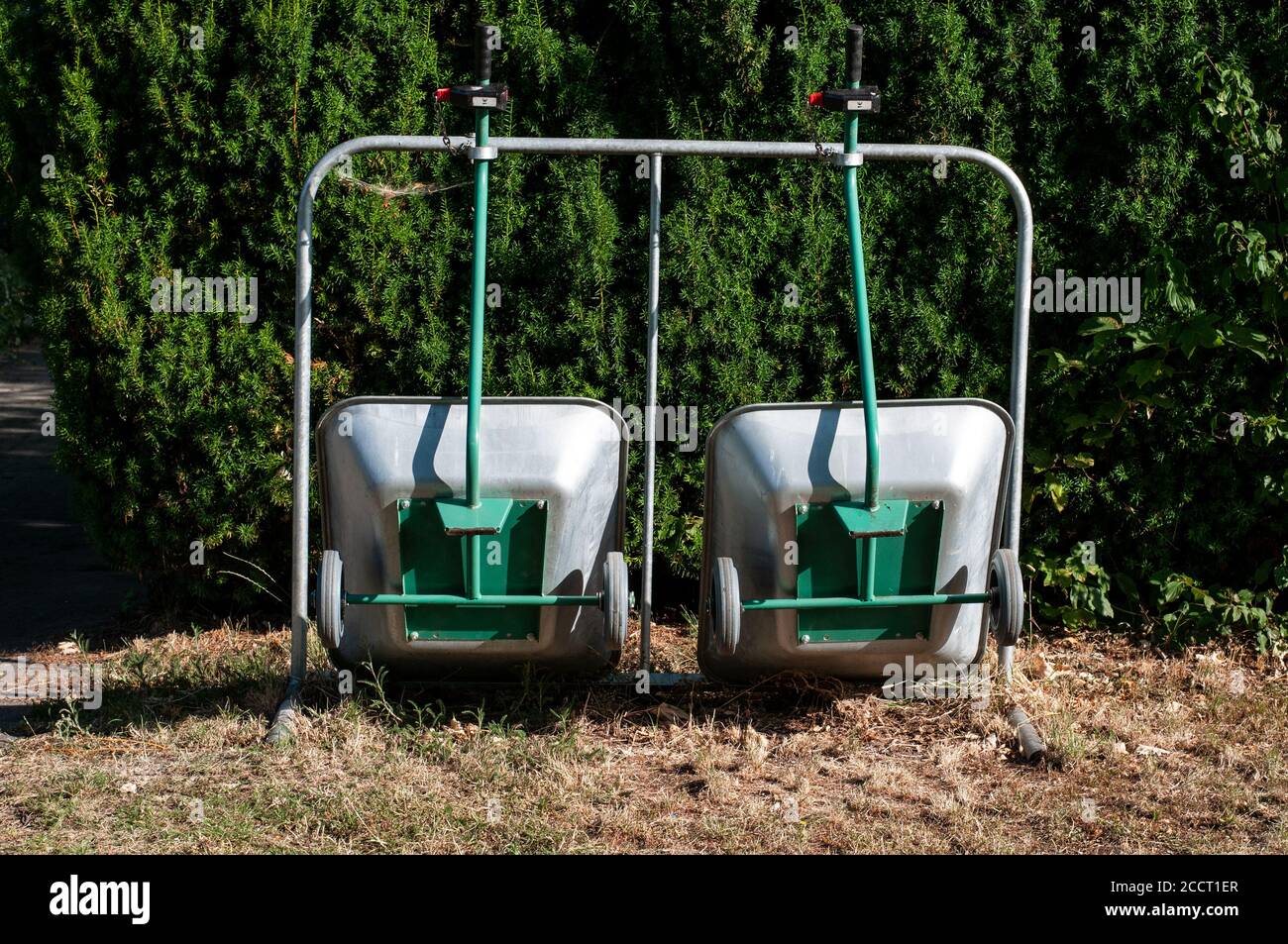 close-up of metal barrows fixed upright next to a yew hedge in a cemetery Stock Photo