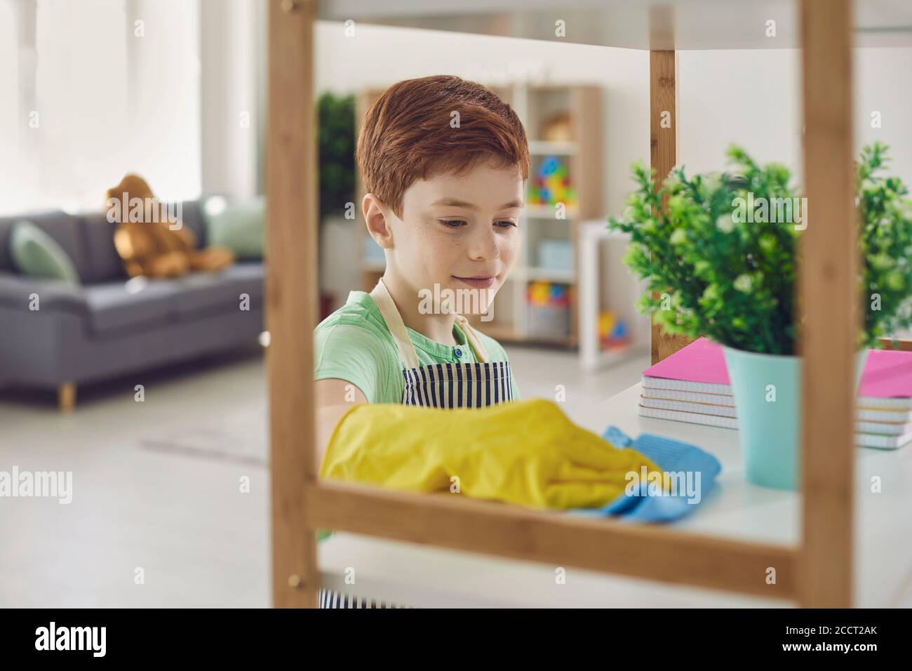 Smiling boy making cleaning and dusting off shelves surfaces at home Stock Photo