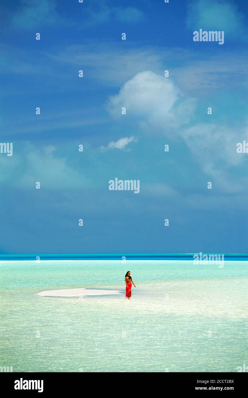 Woman wearing red sarong walking on sandbar in Aitutaki lagoon in the Cook Islands.   South Pacific Stock Photo