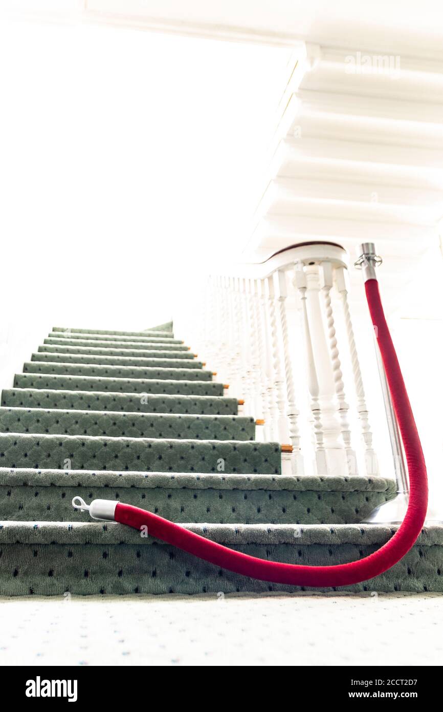 Over exposed, heavenly light at top of ascending staircase; with selective focus on red velvet rope opened on the floor - granting access to the myste Stock Photo