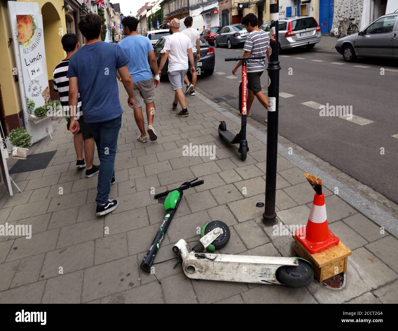 Cracow. Krakow. Poland.Damaged e-scooter tossed on the sidewalk with broken steering column. People passing by. Stock Photo