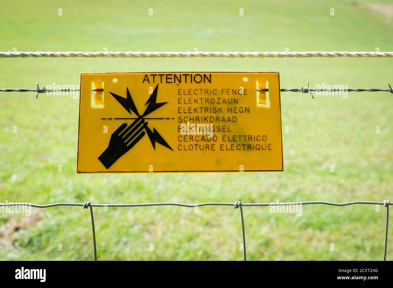Electric fence sign by a field. Stock Photo