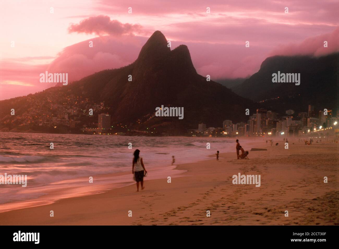 Woman on sandy shores of Ipanema in Rio de Janeiro at sunset with the two mountains called the Dois Irmãos or The Brothers Stock Photo