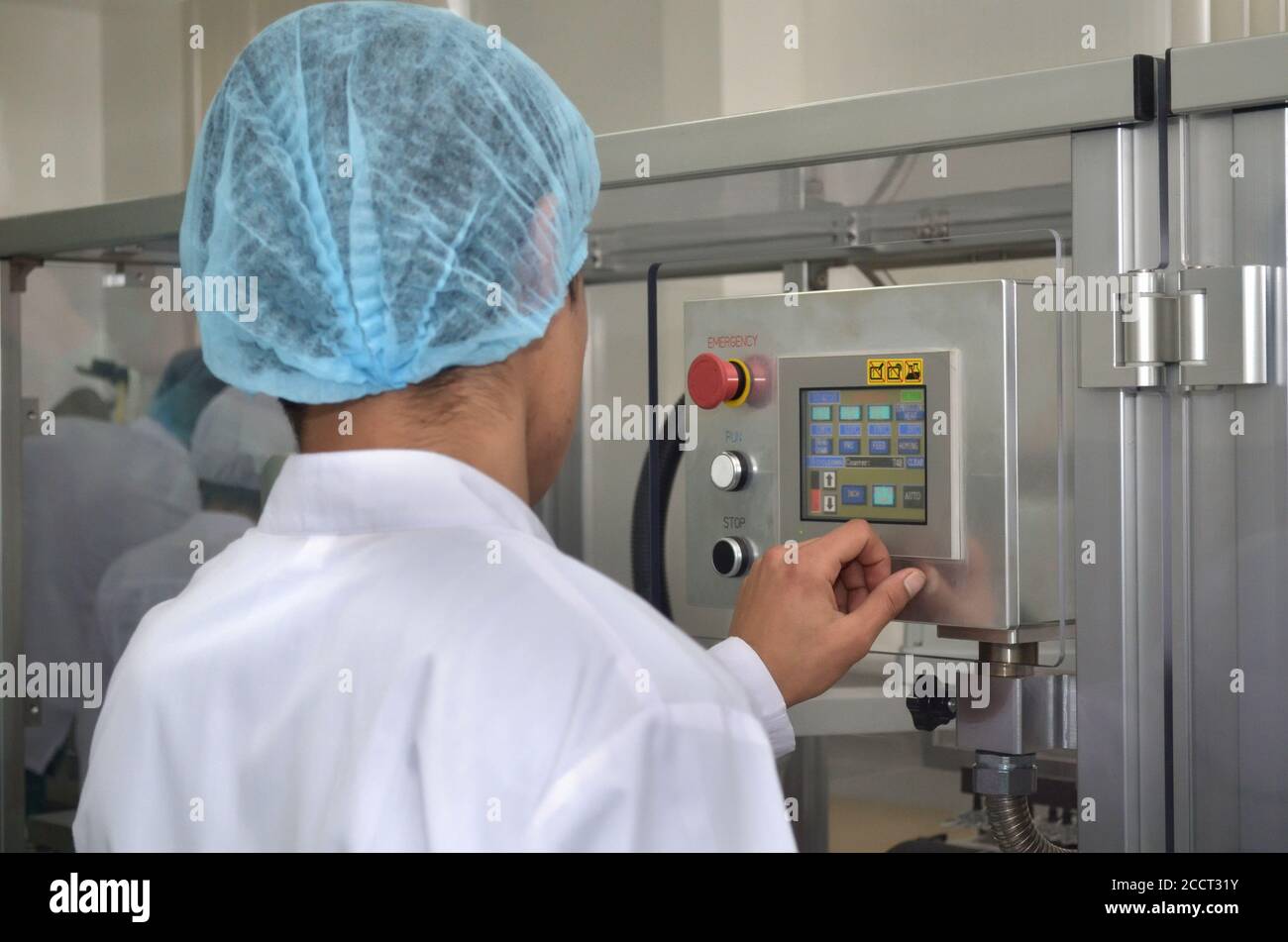 Pharmaceutical industry an employee in a dressing gown and headdress stands at the control panel of an automated production line and manages productio Stock Photo