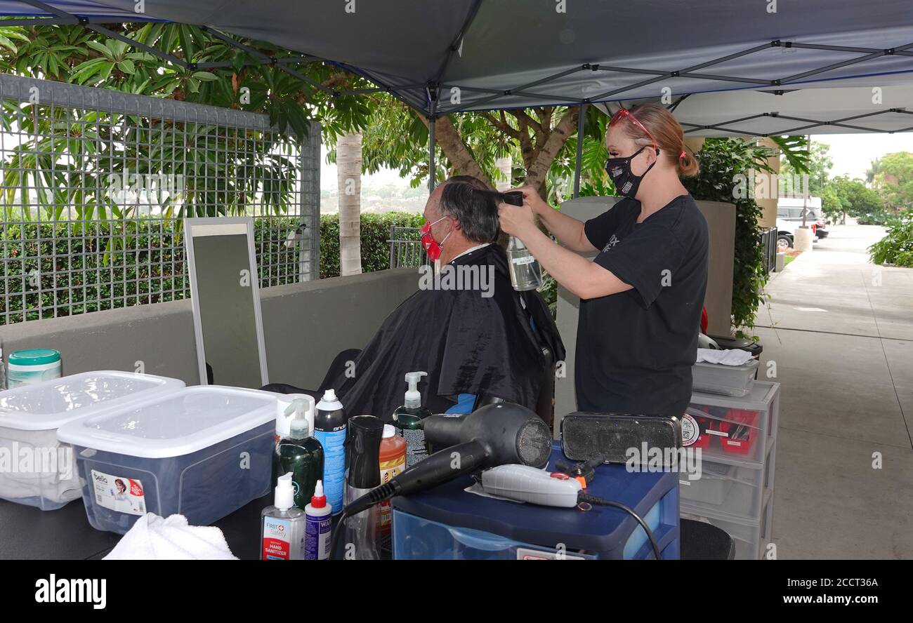 An older man is getting a haircut outside as Sports Clips hair salon moved operations outdoors to avoid Covid-19 shutdown. Stock Photo