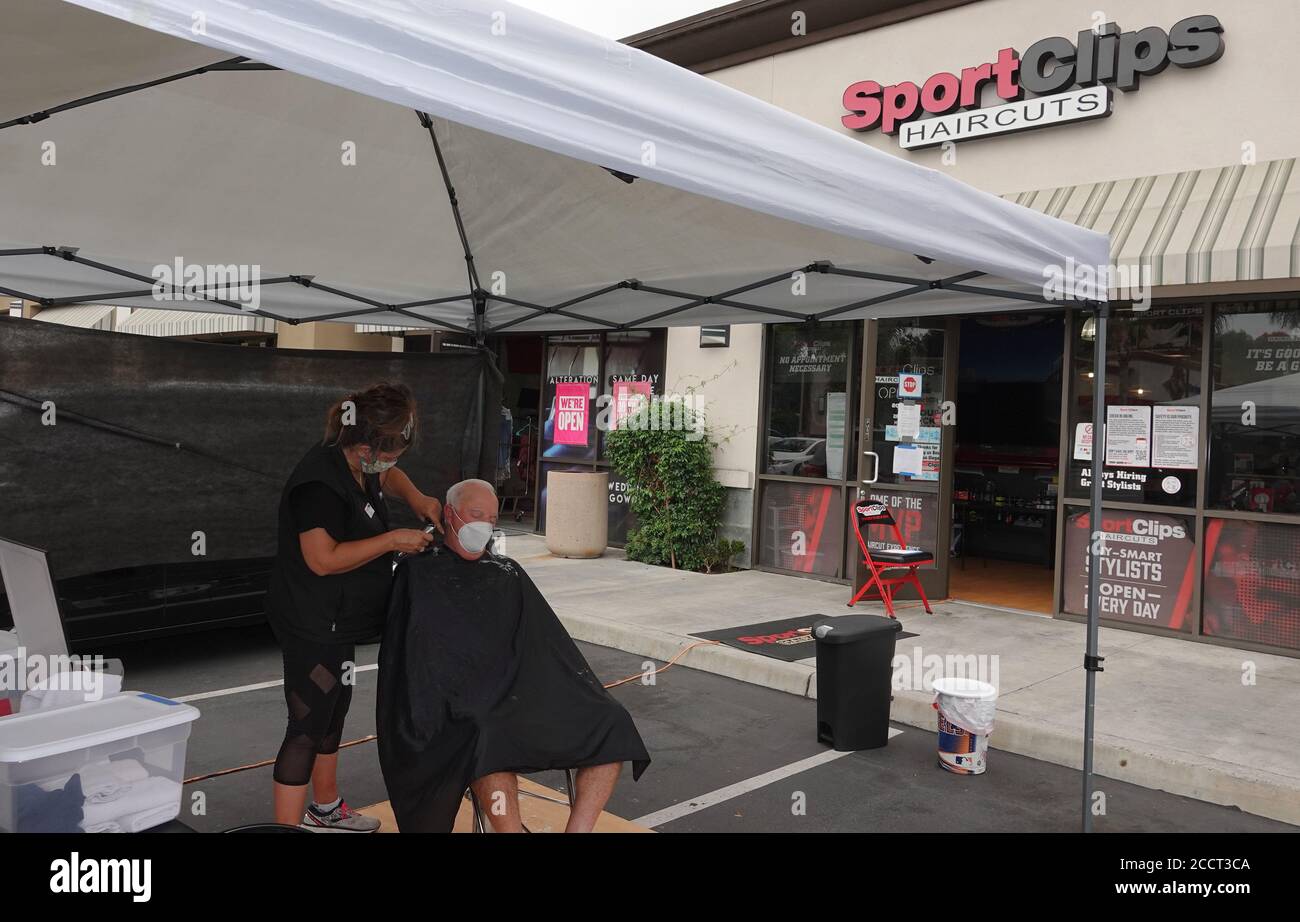 An older man is getting a haircut outside as Sports Clips hair salon moved operations outdoors to avoid Covid-19 shutdown. Stock Photo