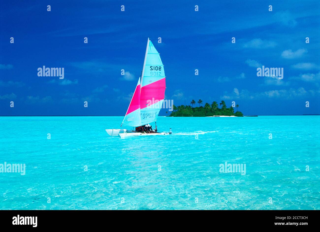 Catamaran flying across aqua waters past deserted island in the Maldives Stock Photo