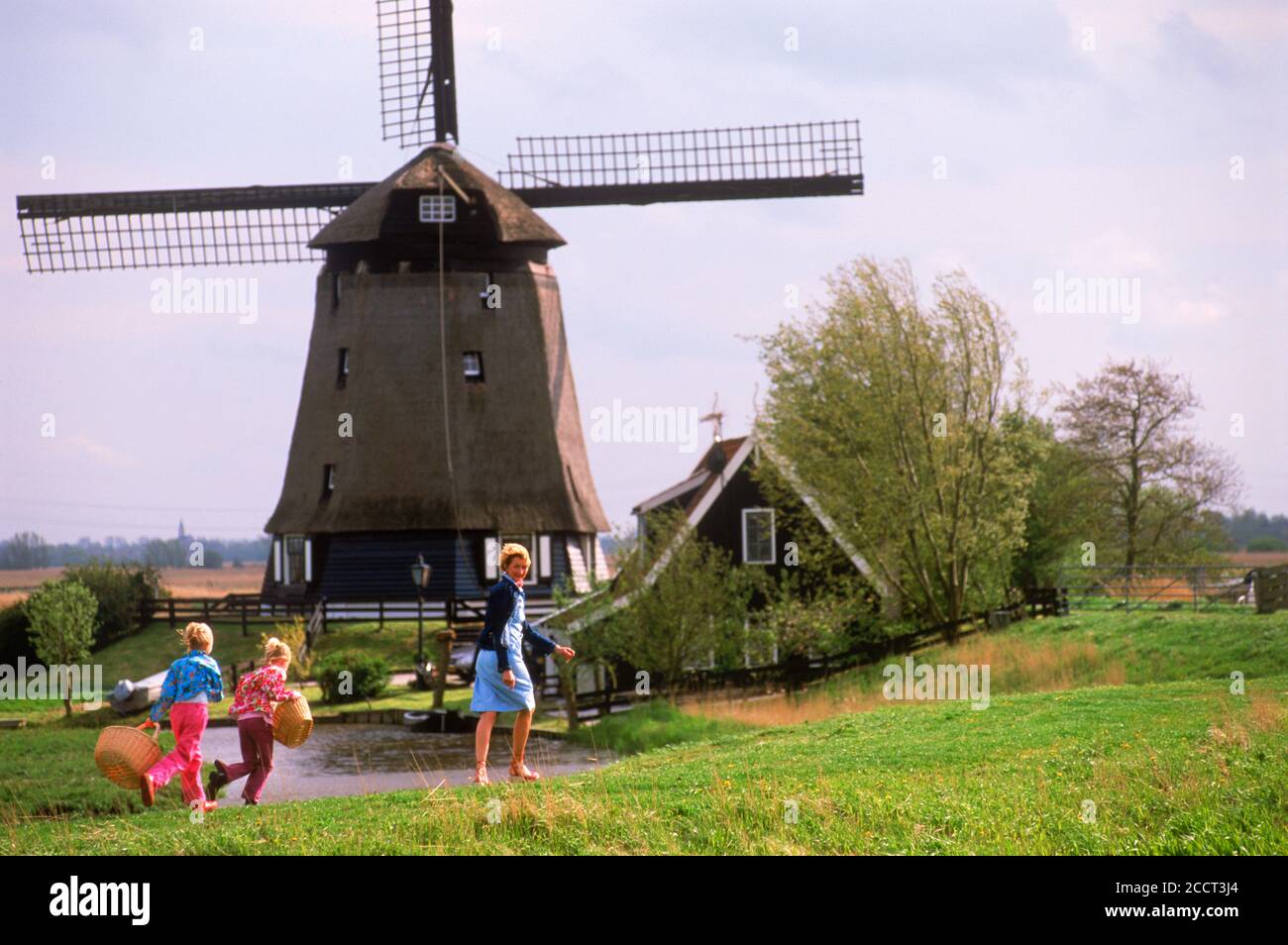 Mother and children with baskets walking home on pathway in Holland near windmill and canal Stock Photo
