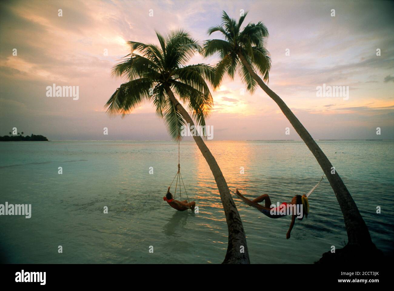 Couple hanging from palm trees over Indian Ocean in the Maldives at sunset Stock Photo