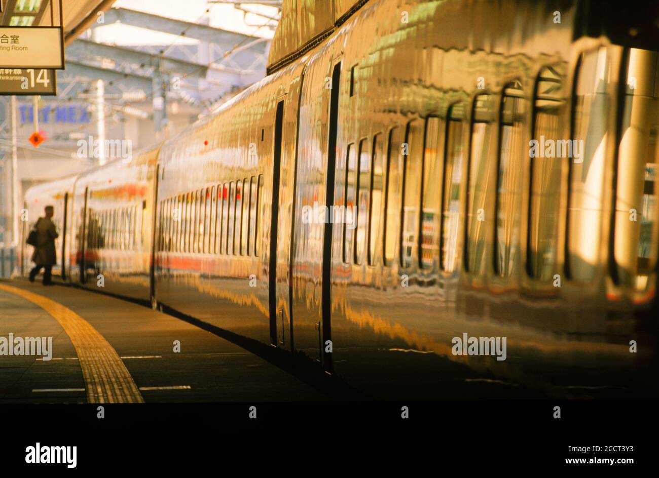 Businessperson boarding Shinkansen bullet train reflecting golden light in Kyoto Station Japan Stock Photo