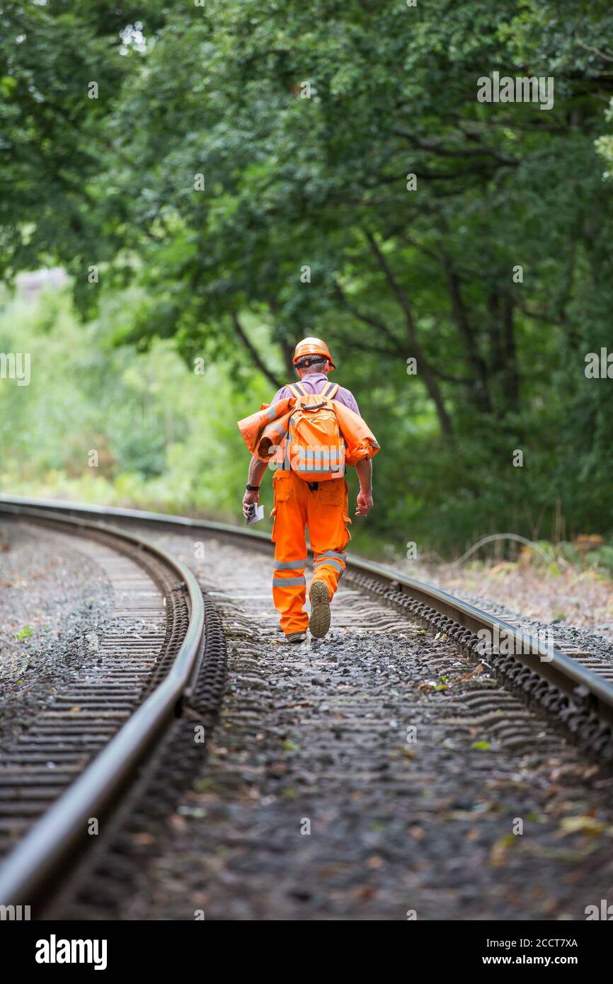 Railway worker, rear, walking isolated along UK heritage railway line inspecting track for damage. Routine railway maintenance, inspection. Stock Photo