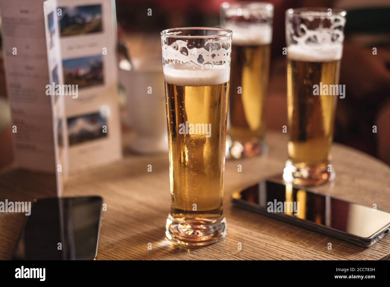 A wooden table in a pub or bar with 3 glasses of gold colored foamy beer and 2 mobile phones. no visible people Stock Photo