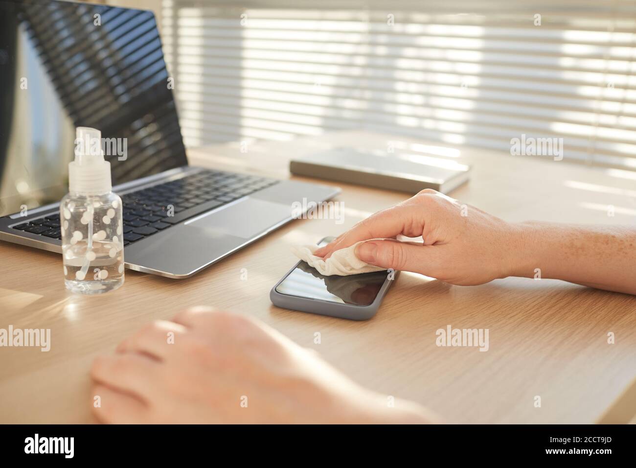 Close up pf female hands sanitizing smartphone while working at desk in post pandemic office, copy space Stock Photo