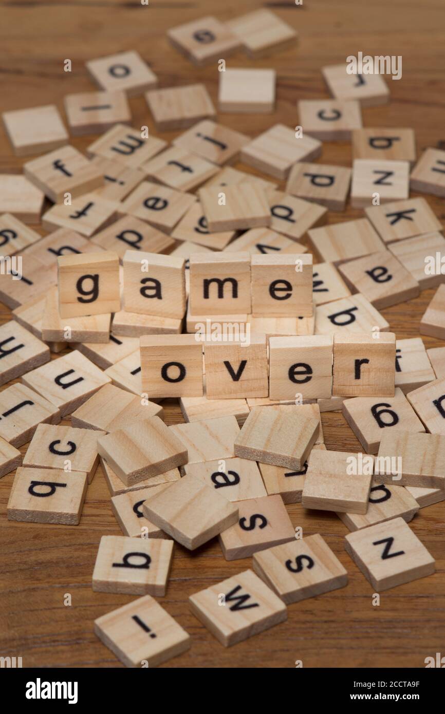 Wooden letters composing the words "game over" on a background of scattered letters spilled on a wooden board Stock Photo