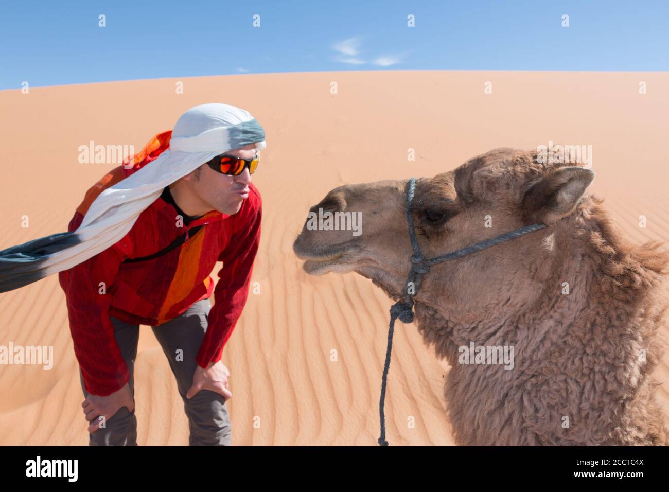 Tourist with turban and sunglasses kissing a camel in the desert dunes. Funny concept Stock Photo