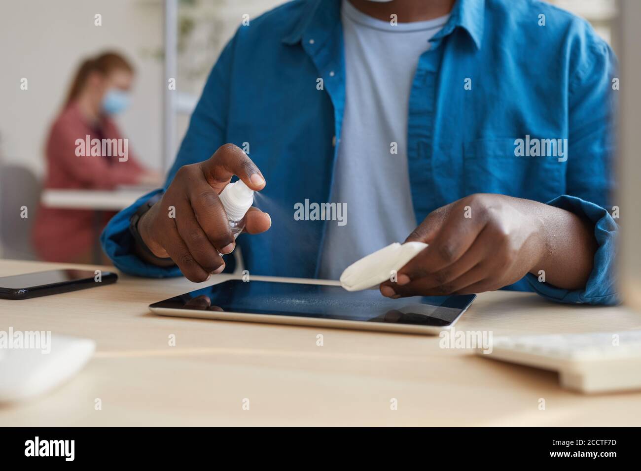 Close up of young African-American man wiping tablet with sanitizing wipes while working at desk in post pandemic office, copy space Stock Photo