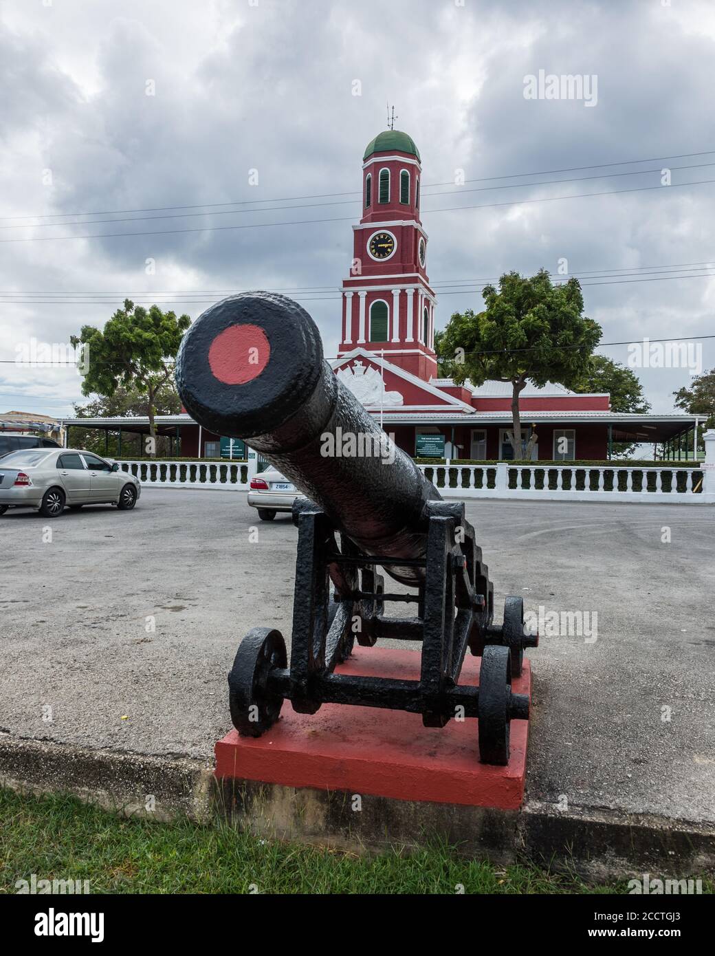 An old cannon in front of he Main Guard, Barbados Garrison, with it's red clock tower. Now headquarters of the Barbados Legion.  Bridgetown, Barbados. Stock Photo