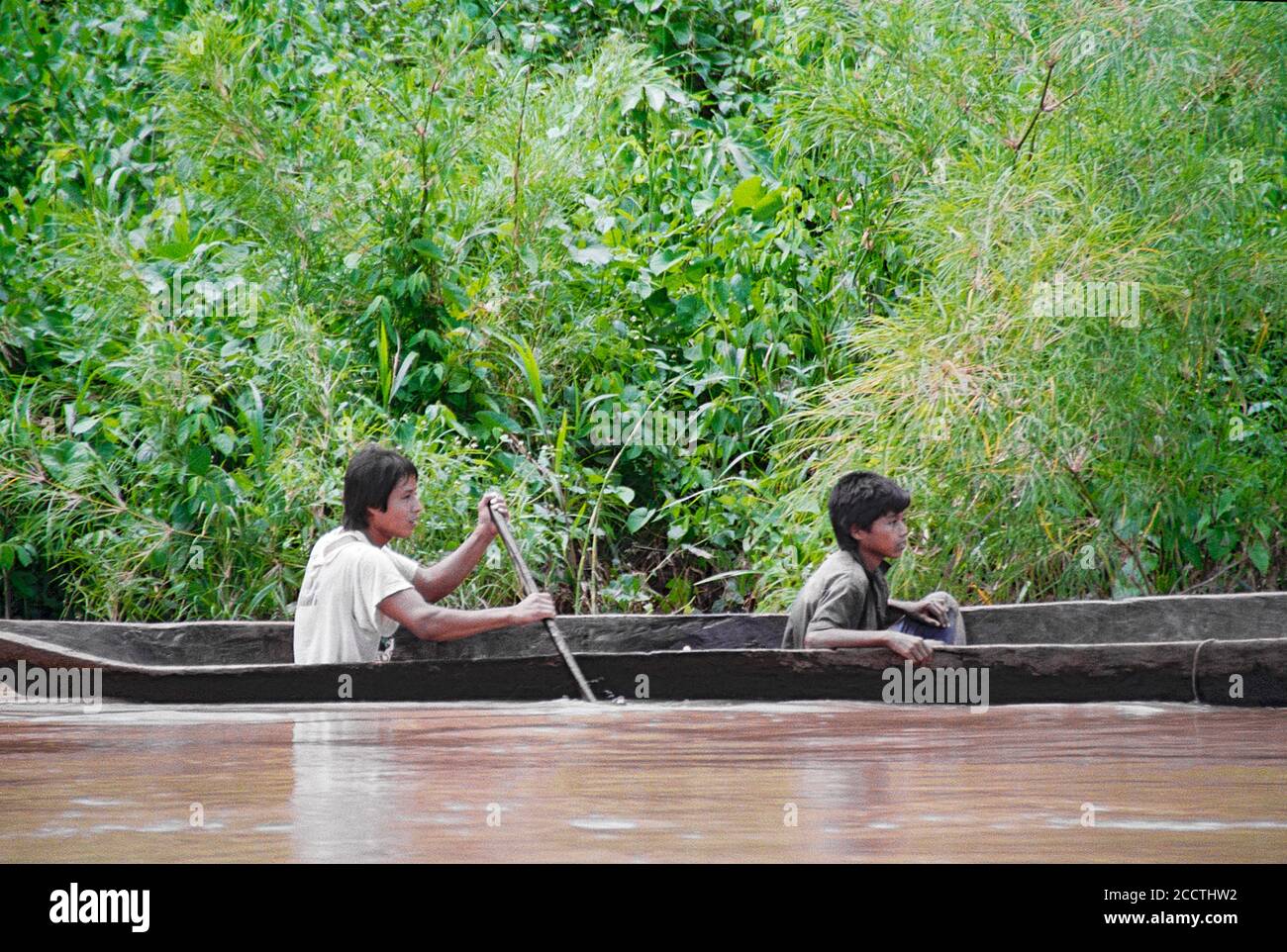 Two young Mayan boys paddle a traditional dugout canoe on the