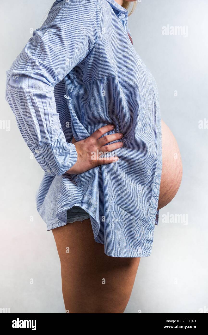 Profile of belly with stretchmarks of pregnant woman in blue shirt on light background Stock Photo