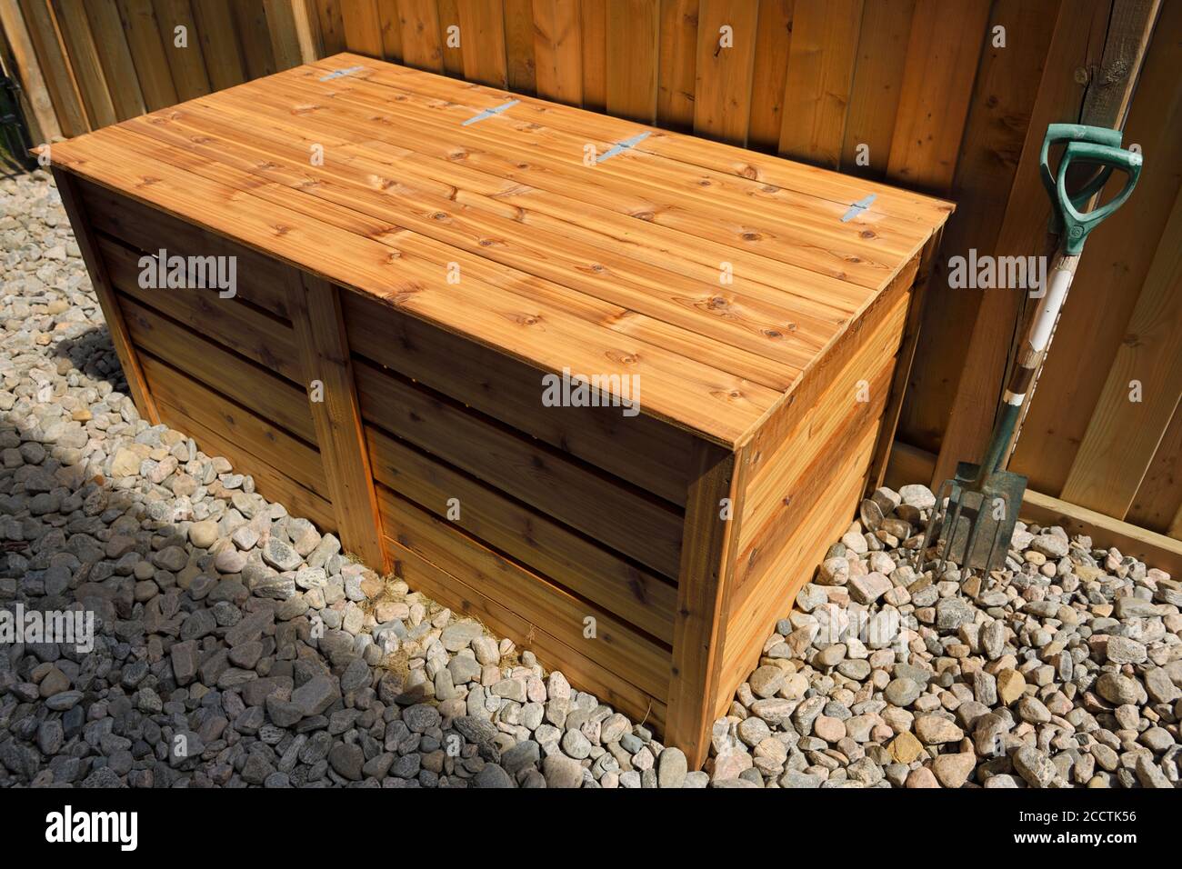 Two bin organic composter made of cedar wood with lid for garden trimmings beside fence on river rocks Stock Photo