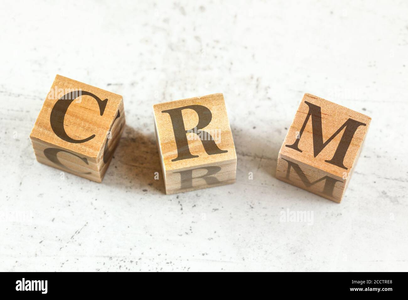 Three wooden cubes with letters CRM - stands for Customer relationship management - on white board. Stock Photo