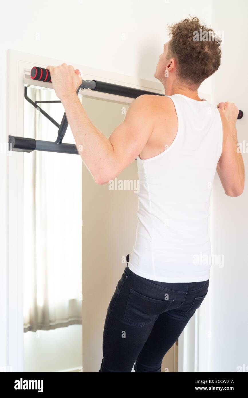 Slim athletic male performing wide grip pull up exercise in doorway, using a pronated or overhand grip, placing emphasis on the muscles in the back. Stock Photo