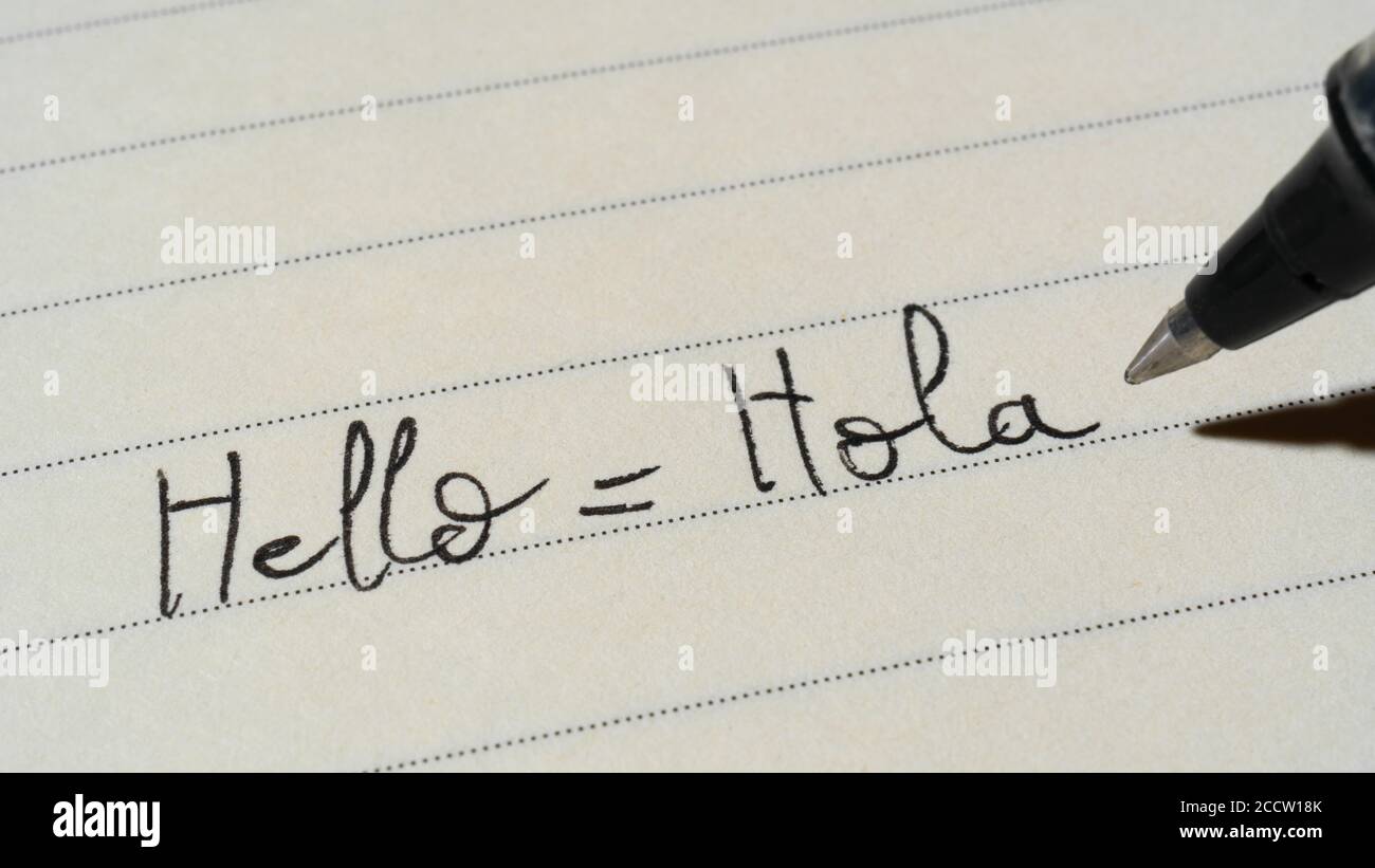 Beginner Spanish language learner writing Hello word Hola for homework on a notebook macro shot Stock Photo