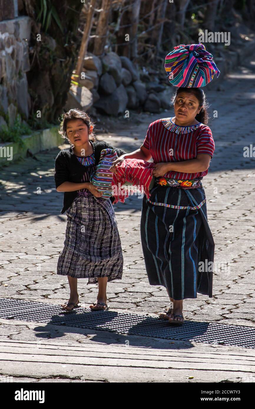 A Cakchiquel Mayan mother and daughter in traditional dress carry their wares to sell in the market in San Marcos la Laguna, Guatemala. Stock Photo