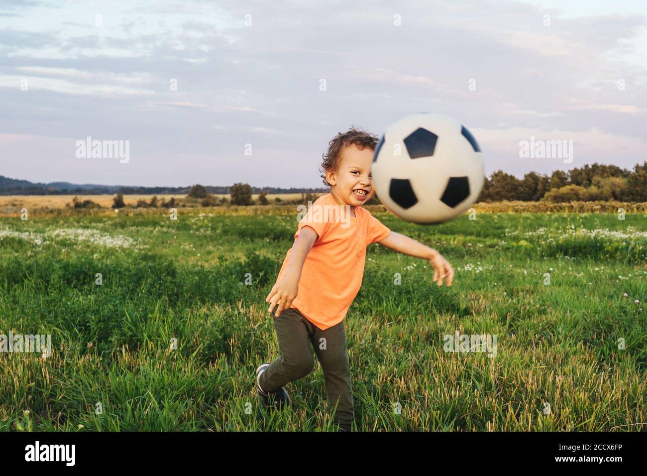 Cute smiling curly Boy kicked a soccer ball in the field Stock Photo
