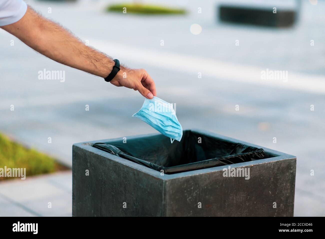 Man throwing used disposable protective surgical mask into the garbage bin closeup Stock Photo