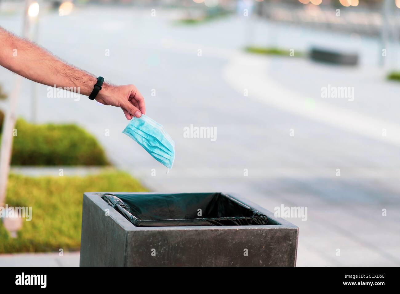 Man throwing used disposable protective surgical mask into the garbage bin closeup Stock Photo
