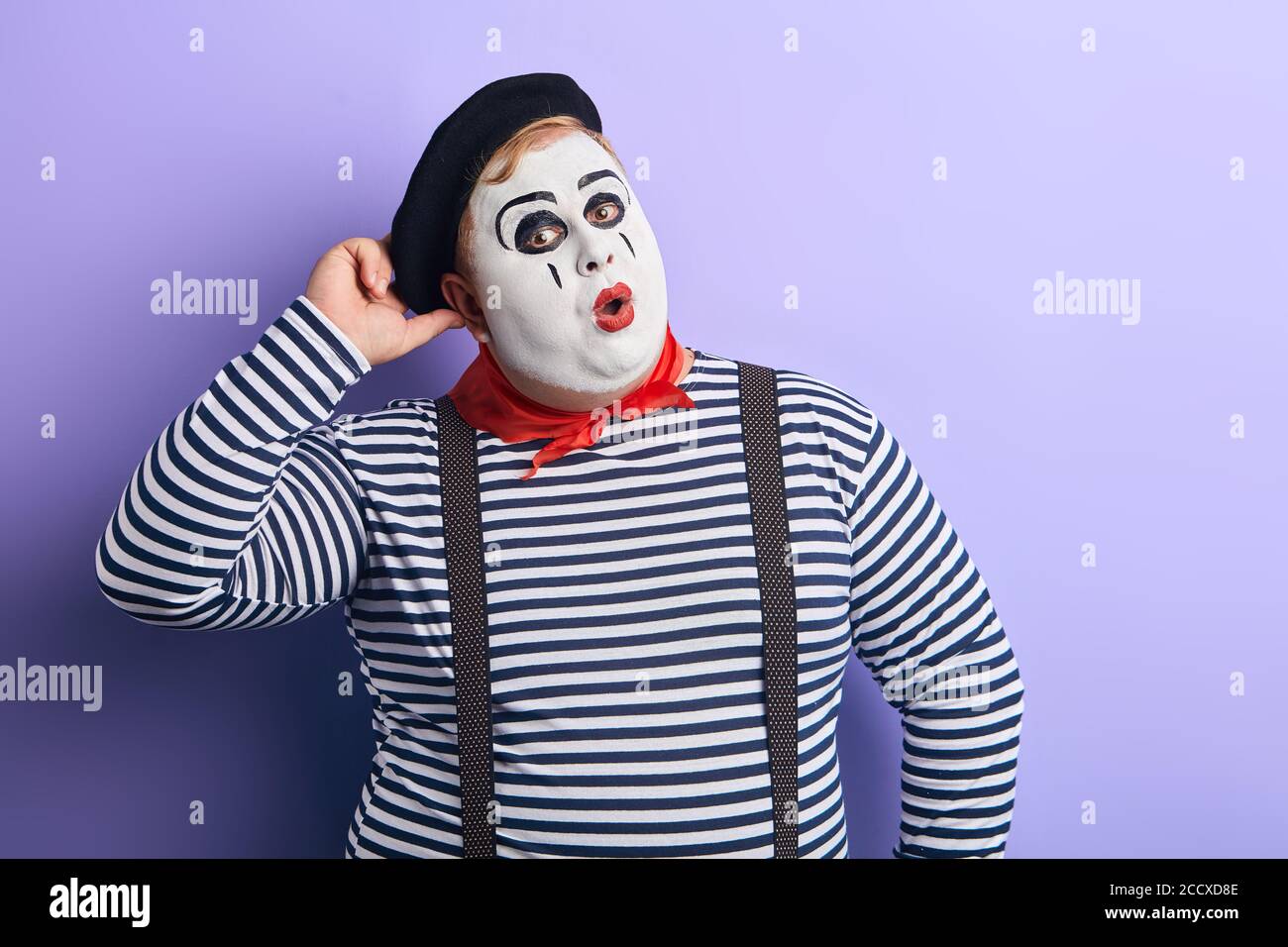 thoughtful clown in striped sweater, suspender and hat with hand on his head solving problem. close up portrait, isolated blue background, studio shot Stock Photo