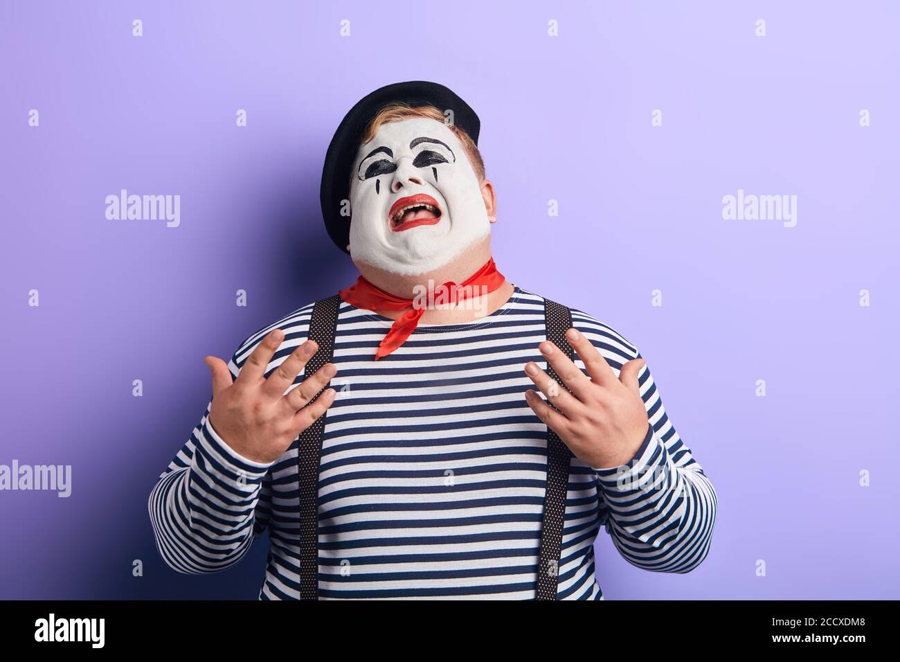 close up of a sad , upset , depressed crying clown with raised arms looking up, isolated blue background, studio shot Stock Photo