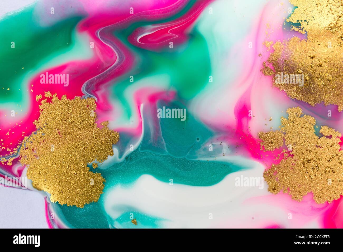 Pink, gold and green mixed inks spilled on white paper background
