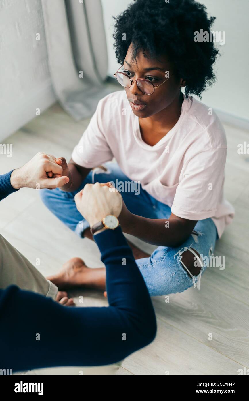 Caucasian boyfriend and his african girlfriend practice yoga, sit crossed legs, holding hands together, looking at each other while sitting on wooden Stock Photo