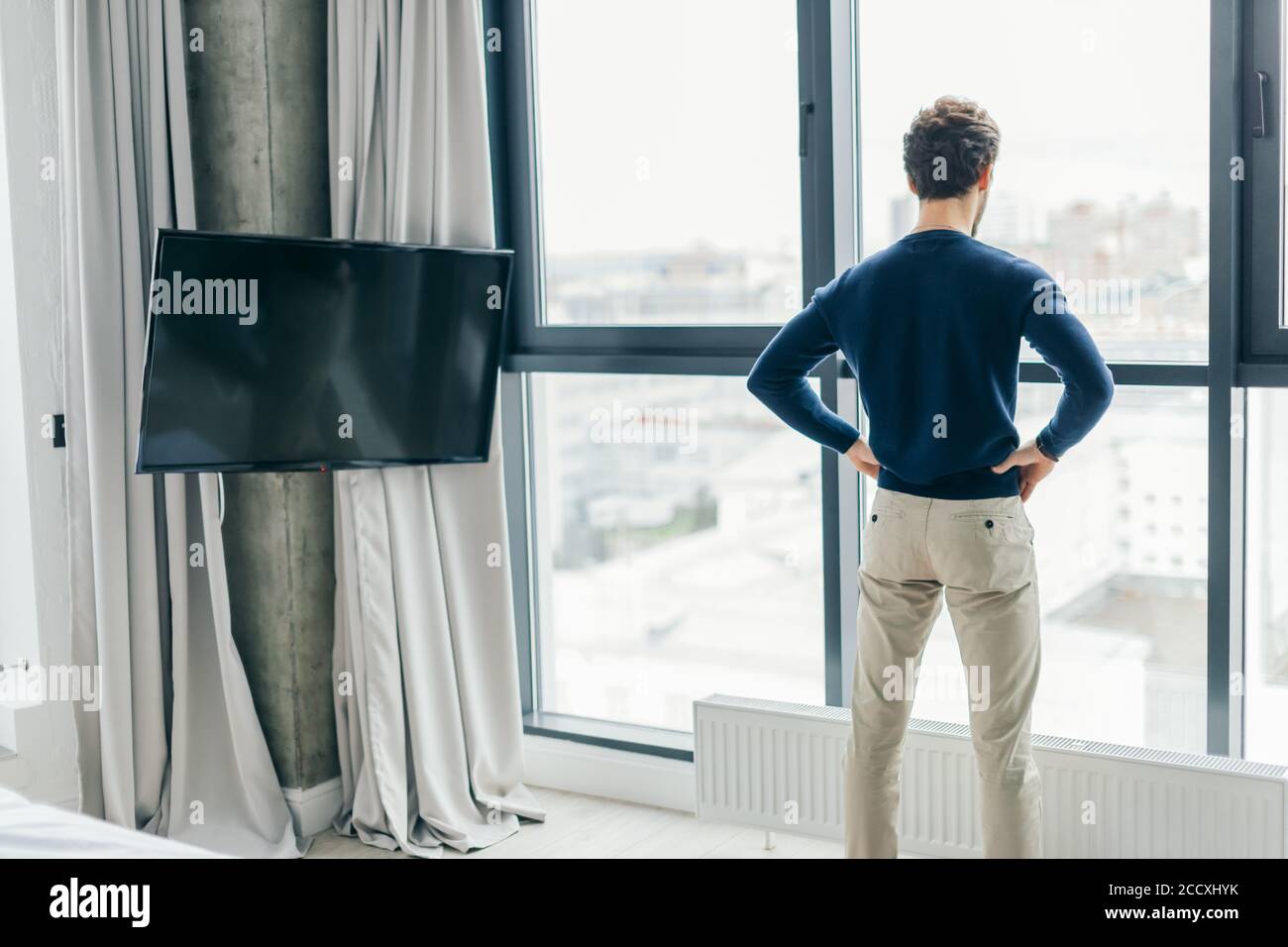 Caucasian athletic man dressed in casual clothes, standing near the  panoranic window in the modern interior room, backside view Stock Photo -  Alamy