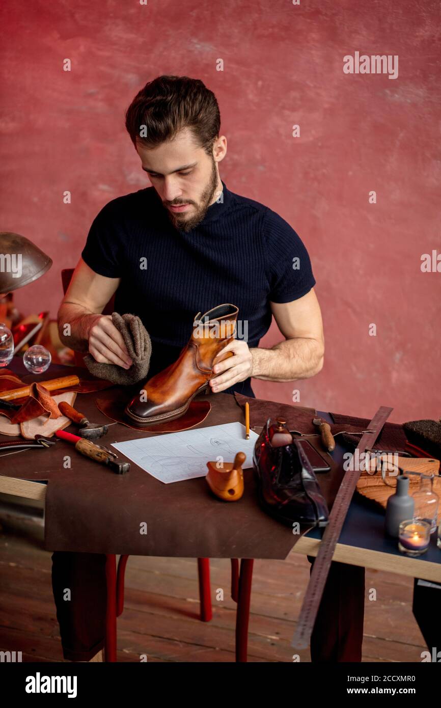 serious workman giving leather boots a high polish in close