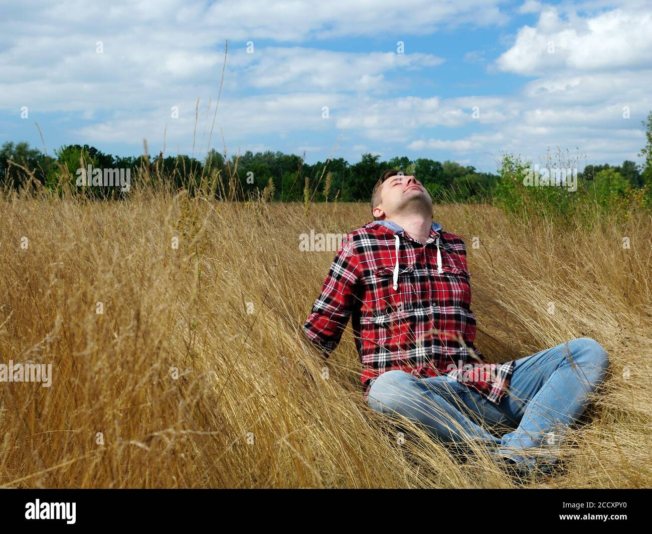 Young guy is sitting in the autumn grass. Relaxation and tourism in nature. Stock Photo