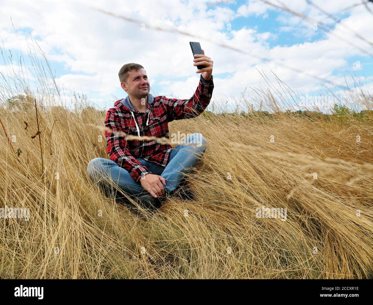 Young tourist takes a selfie while sitting in the autumn field. Stock Photo