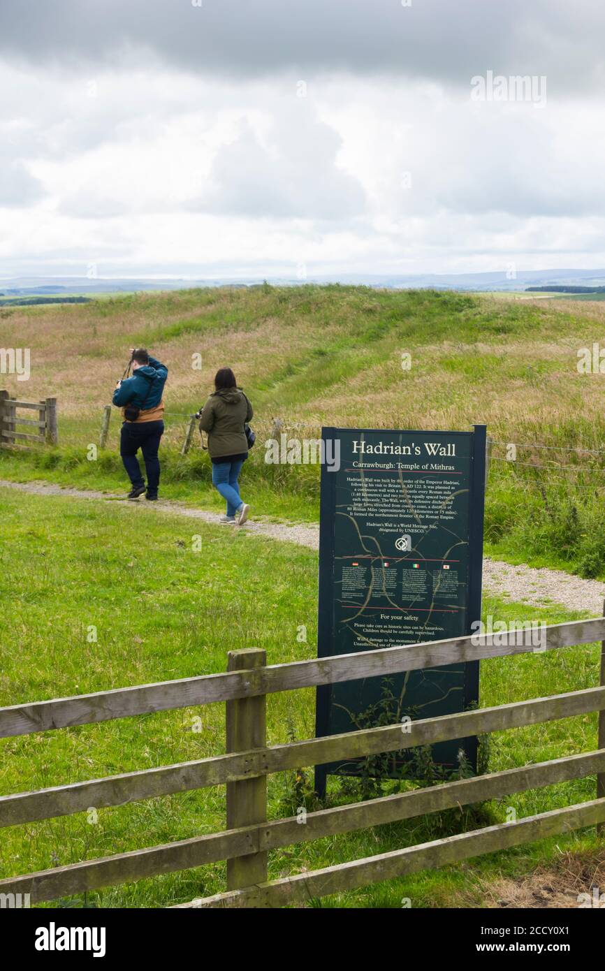 Two people walking along the footpath at Brocolitia Temple of Mithras, a Mithraeum, near the site of the Roman fort of Carrawburgh, Northumberland. Stock Photo