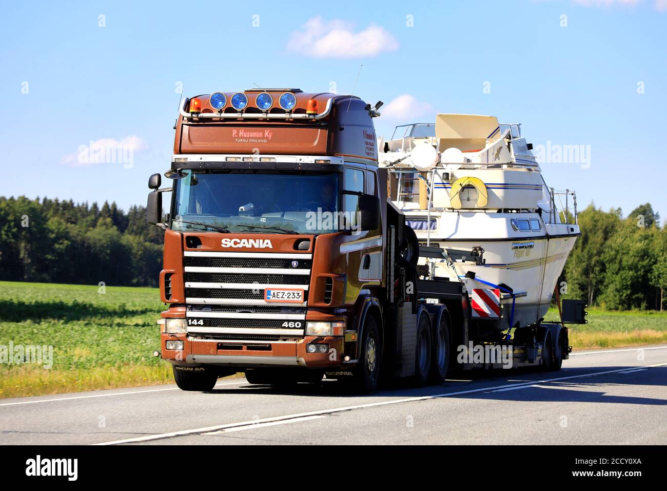 Brown Scania 144 460 semi trailer of P Husonen Ky transports recreational boat on highway 10 as oversize load. Tammela, Finland. August 21, 2020. Stock Photo