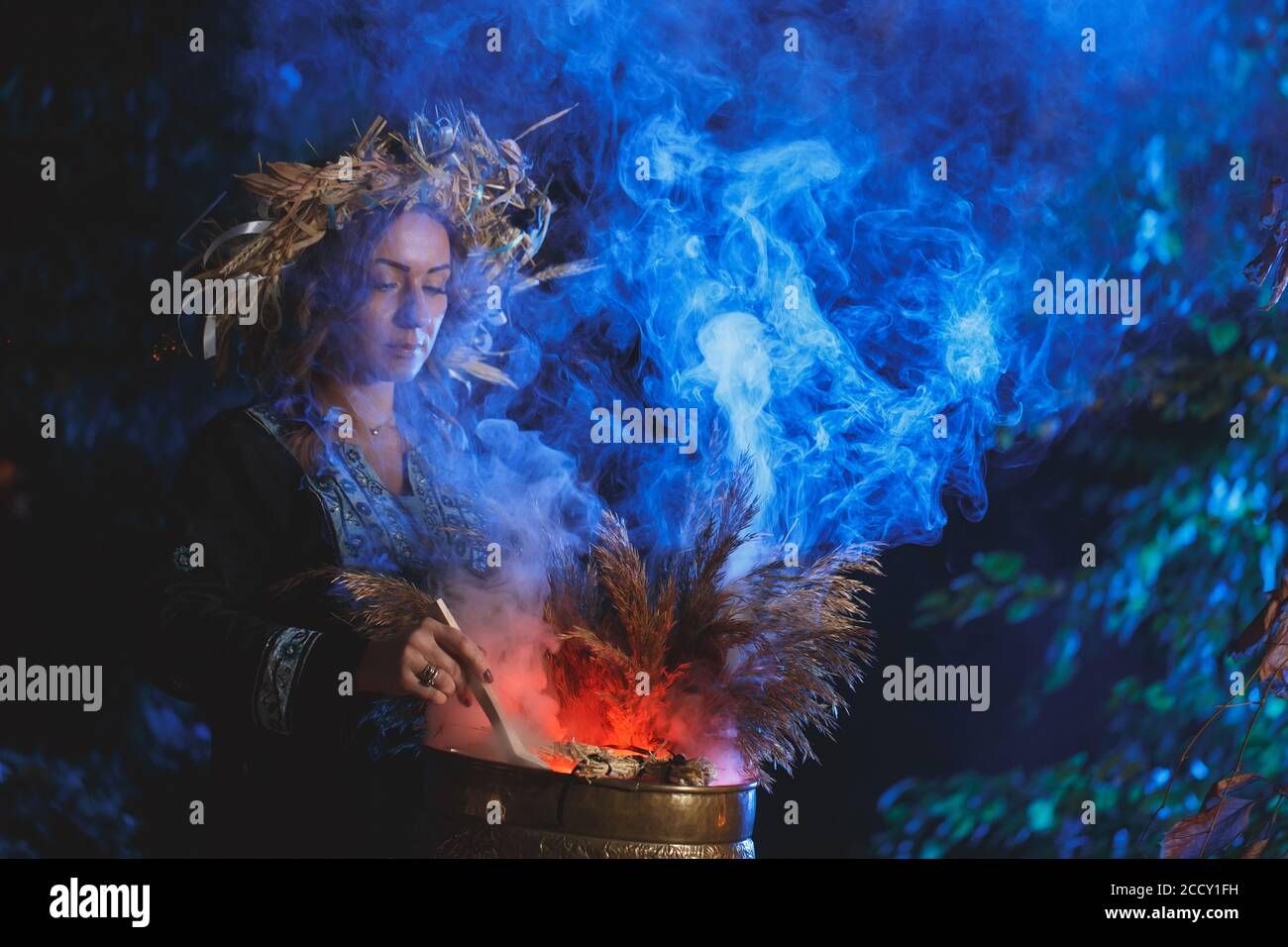 A forest witch brews a potion holding a Voodoo doll. Stock Photo