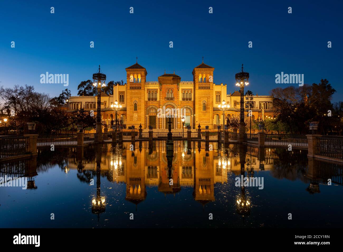 Illuminated art museum Museo de Artes y Costumbres Populares de Sevilla reflected in a fountain, blue hour, Plaza de America, Seville, Andalusia Stock Photo
