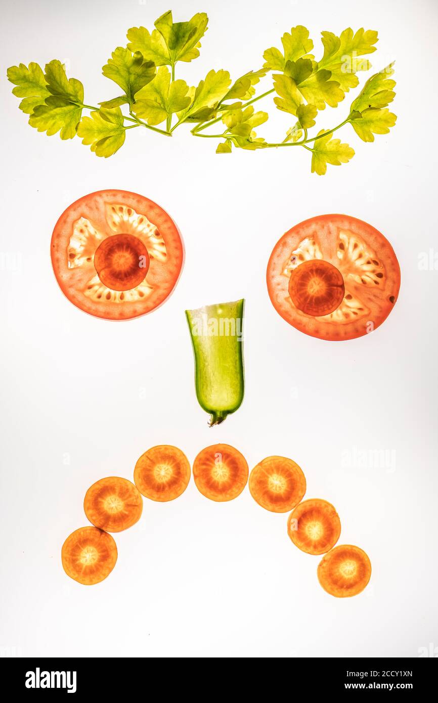 Sad face of vegetables, smiley face, slices of cucumber, carrot and tomato with parsley, white background, food photography Stock Photo