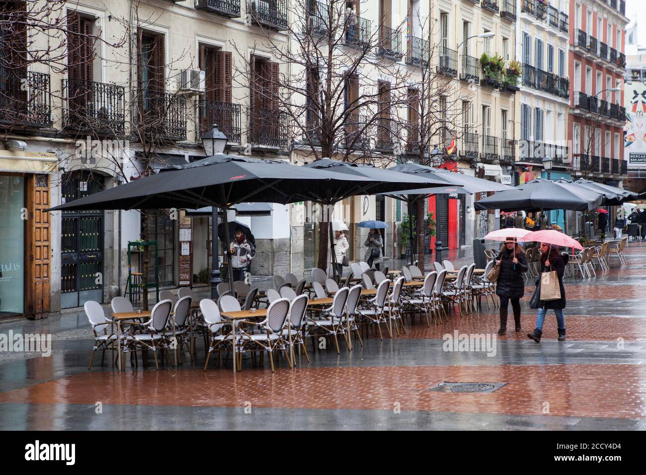 Empy seats in terraces of chueca square in the gay district as people walks by on a rainy day, Madrid Stock Photo