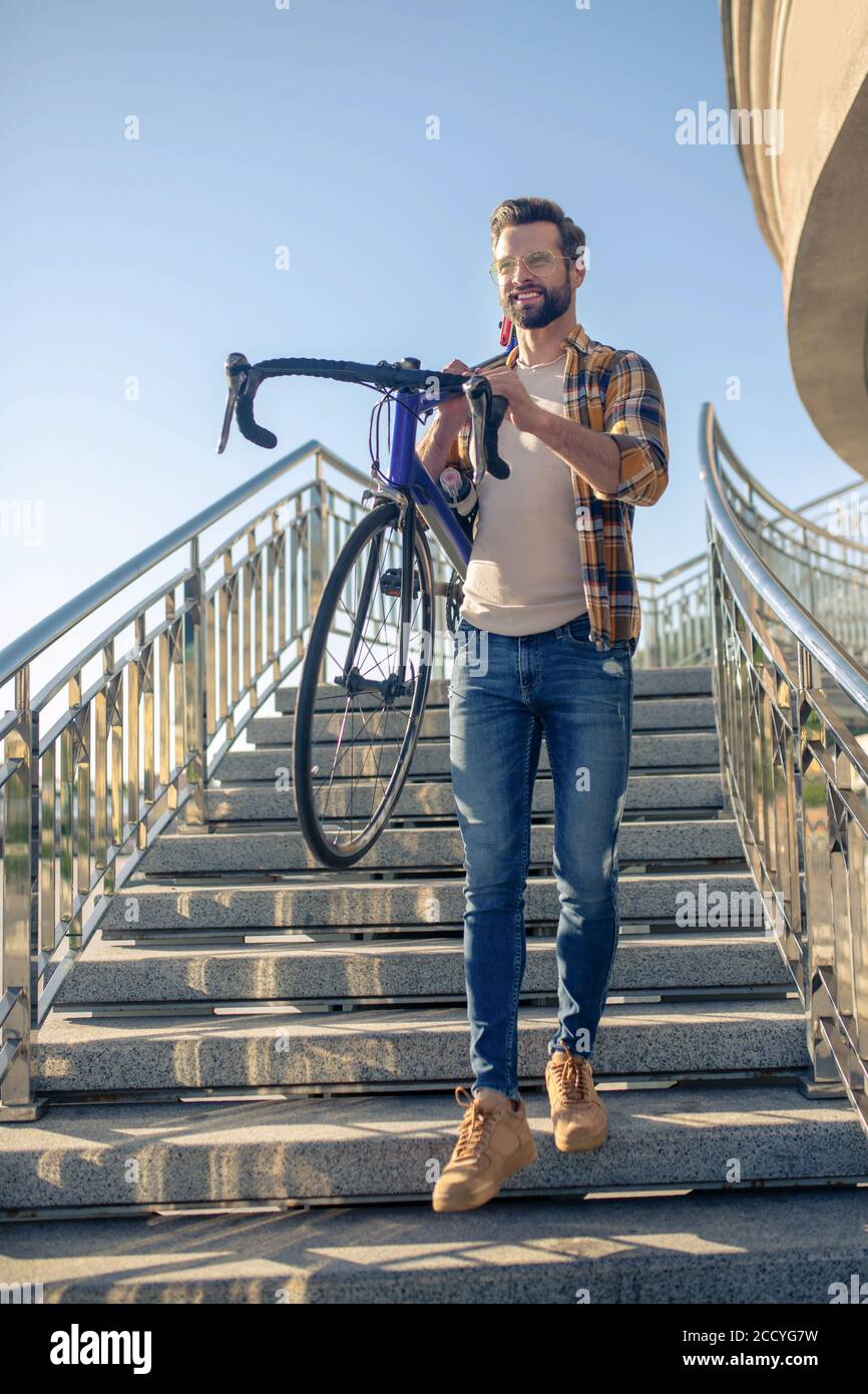 Energetic smiling man carrying bike down stairs Stock Photo