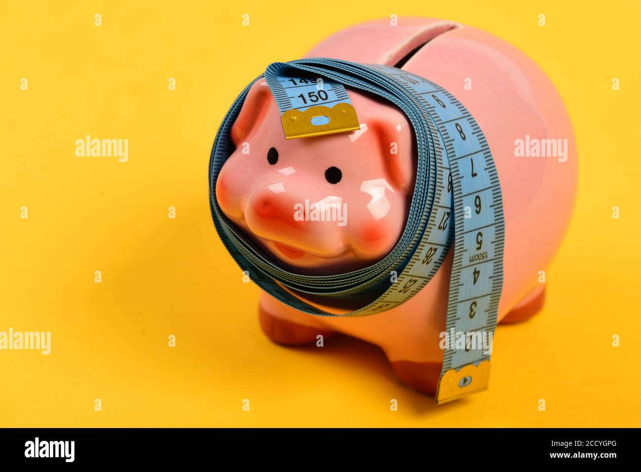 Ceramic toy pig with blue flexible ruler on yellow background. Piggy ...